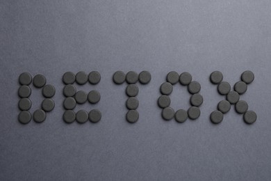 Word Detox made with activated charcoal pills on dark background, flat lay. Natural sorbent