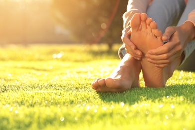 Young woman sitting barefoot on fresh green grass outdoors, closeup