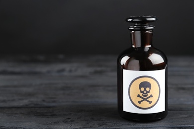 Glass bottle of poison with warning sign on black wooden table. Space for text