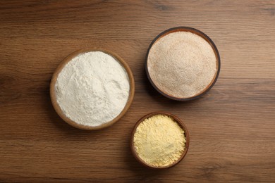 Different types of flours in bowls on wooden table, flat lay