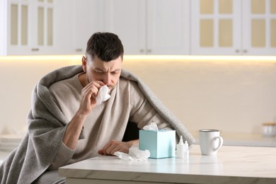 Ill man at table with nasal spray, drops and box of paper tissues in kitchen