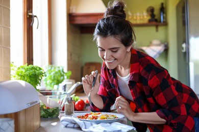 Young woman with plate of freshly fried eggs and vegetables at countertop in kitchen