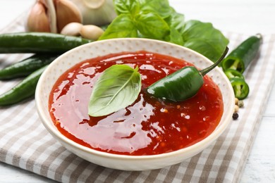Spicy chili sauce with basil on white table