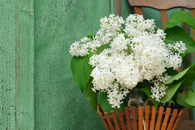 Beautiful lilac flowers in wooden basket near green wall. Space for text
