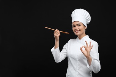Photo of Happy female chef with wooden spoon showing ok gesture on black background. Space for text