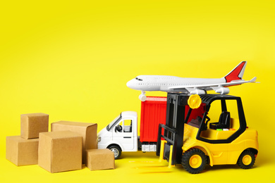 Different toy vehicles with boxes on yellow background. Logistics and wholesale concept