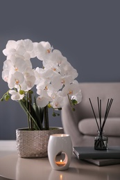 Beautiful orchid, burning candles and air reed freshener on table indoors