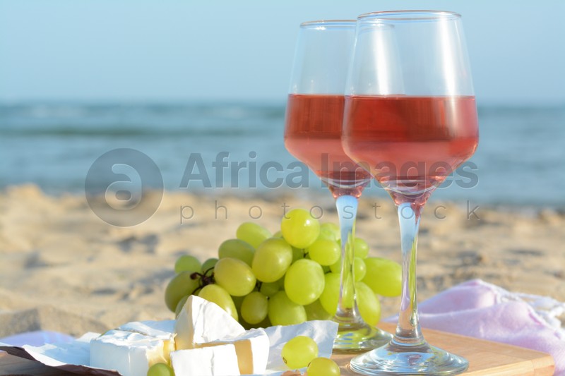Glasses with rose wine and snacks on sandy seashore, closeup. Space for text