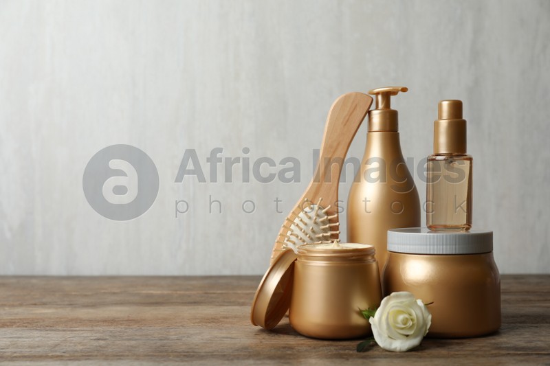 Different hair products, flower and brush on wooden table. Space for text