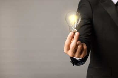 Glow up your ideas. Closeup view of businessman holding light bulb on grey background, space for text