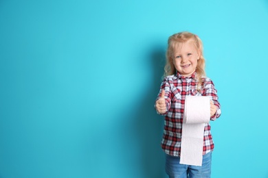 Cute little girl holding toilet paper roll on color background. Space for text
