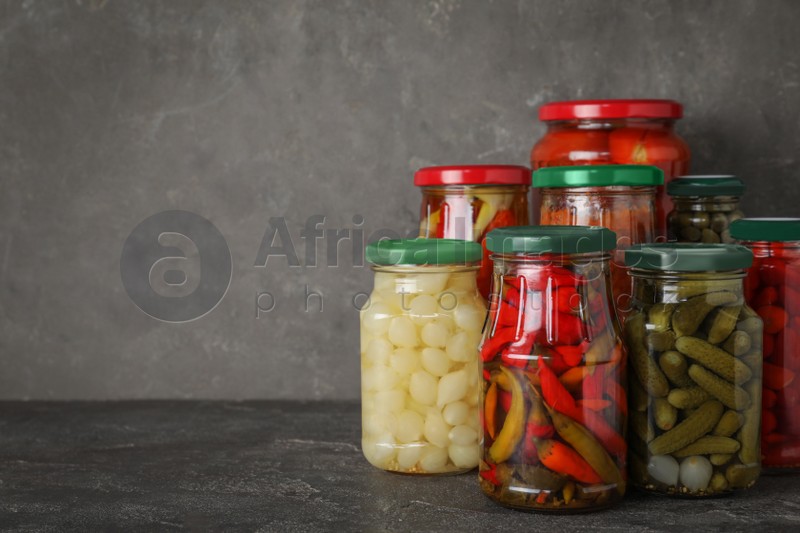 Jars of tasty pickled vegetables on grey table. Space for text