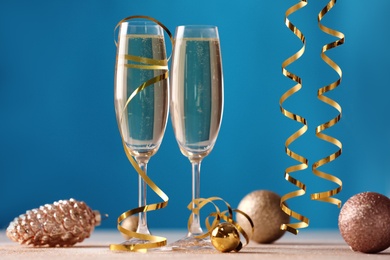 Glasses of champagne with serpentine streamers and Christmas ornaments on table against blue background