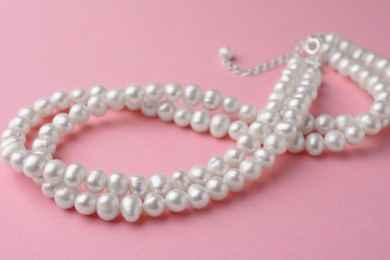 Photo of Elegant necklace with pearls on pink background, closeup