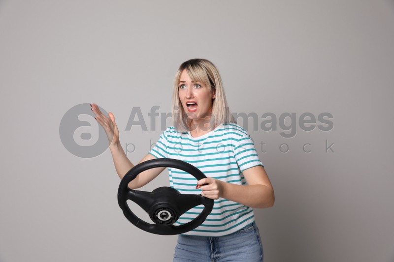 Emotional woman with steering wheel on grey background