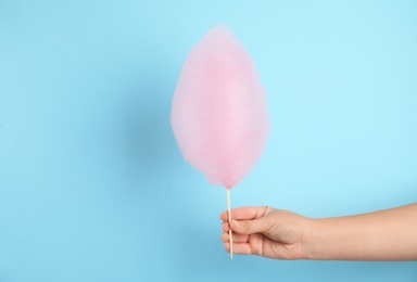 Woman holding sweet pink cotton candy on light blue background, closeup view