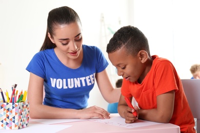 Little African-American boy learning alphabet with volunteer at table indoors