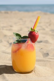 Glass of refreshing drink with strawberry on sandy beach near sea