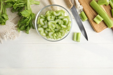 Photo of Cut fresh green celery in bowl on white wooden table, flat lay. Space for text