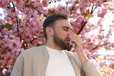 Man suffering from seasonal pollen allergy near blossoming tree outdoors