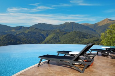 Chaise longues near outdoor swimming pool at resort and beautiful view of mountains on sunny day
