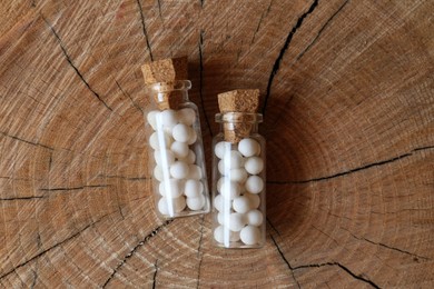 Bottles with homeopathic remedy on wooden stump, flat lay