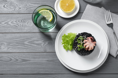 Delicious black risotto with baby octopus served on grey wooden table, flat lay