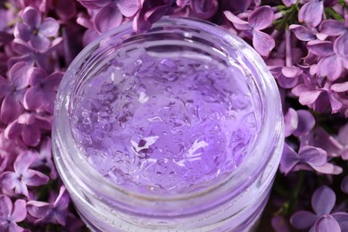 Photo of Jar of cosmetic product and lilac flowers as background, closeup