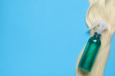 Photo of Spray bottle with thermal protection and lock of blonde hair on light blue background, flat lay. Space for text
