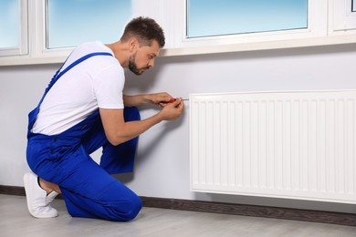 Professional plumber using screwdriver while preparing heating radiator for winter season indoors