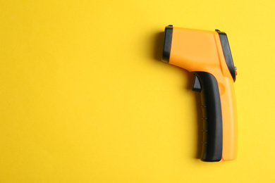 Modern non-contact infrared thermometer on yellow background, top view. Space for text