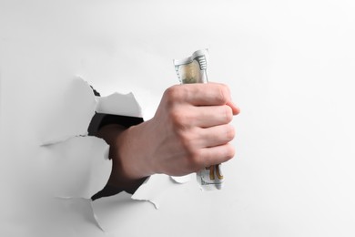 Man breaking through white paper with money in fist, closeup
