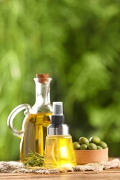 Bottles with cooking oil, olives and rosemary on wooden table against blurred background