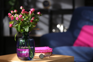 Glass vase with fresh flowers and wristwatch on wooden table. Space for text