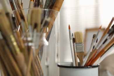 Holders with different paintbrushes in studio, closeup. Artist's workplace