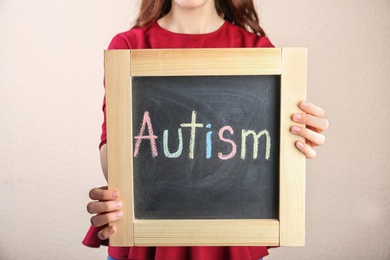 Woman holding chalkboard with word AUTISM on light background