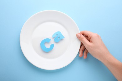 Woman holding plate with calcium symbol made of letters on light blue background, top view