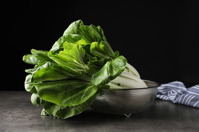 Fresh green pak choy cabbages with water drops in sieve on grey table