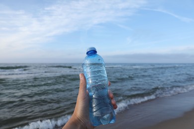Photo of Woman holding plastic bottle with water near sea, closeup