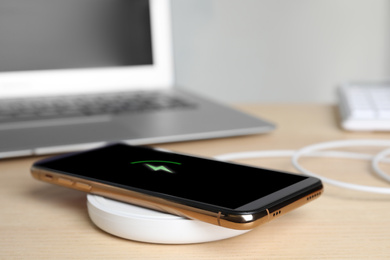 Mobile phone charging with wireless pad on wooden table, closeup. Space for text