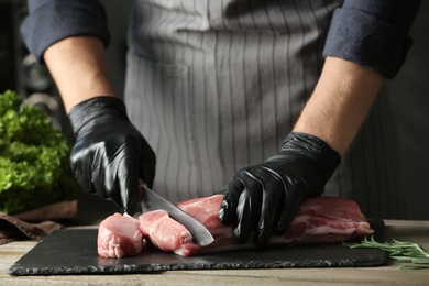 Photo of Man cutting fresh raw meat on wooden table, closeup