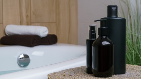 Bottle of bubble bath and cosmetic products on wicker mat near tub indoors, space for text