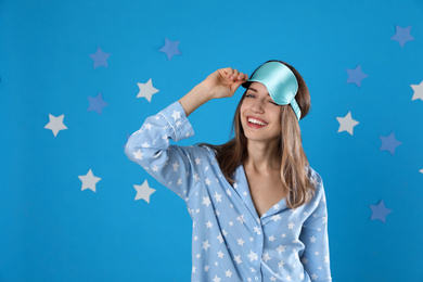 Beautiful woman wearing pajamas and sleep mask on light blue background. Bedtime