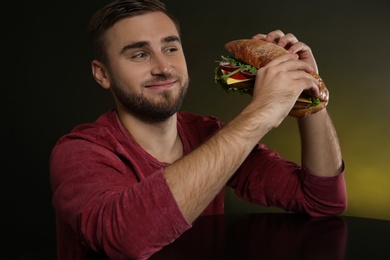 Young hungry man with tasty burger on color background