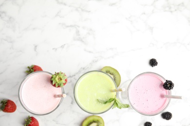 Tasty fresh milk shakes with fresh berries on white marble table, flat lay. Space for text