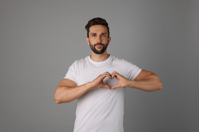 Photo of Man making heart with hands on grey background