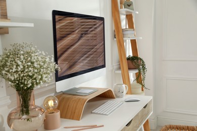 Comfortable workplace with modern computer and beautiful flowers in room. Interior design