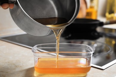 Photo of Woman pouring used cooking oil from saucepan into container on kitchen counter, closeup