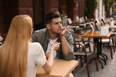 Man getting bored during first date with overtalkative young woman at outdoor cafe