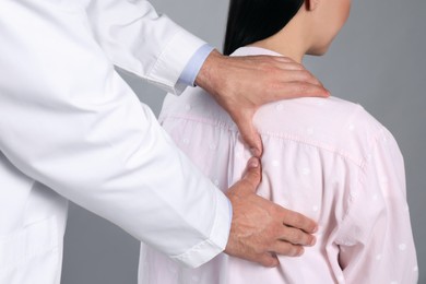 Doctor examining woman with shoulder pain on grey background, closeup